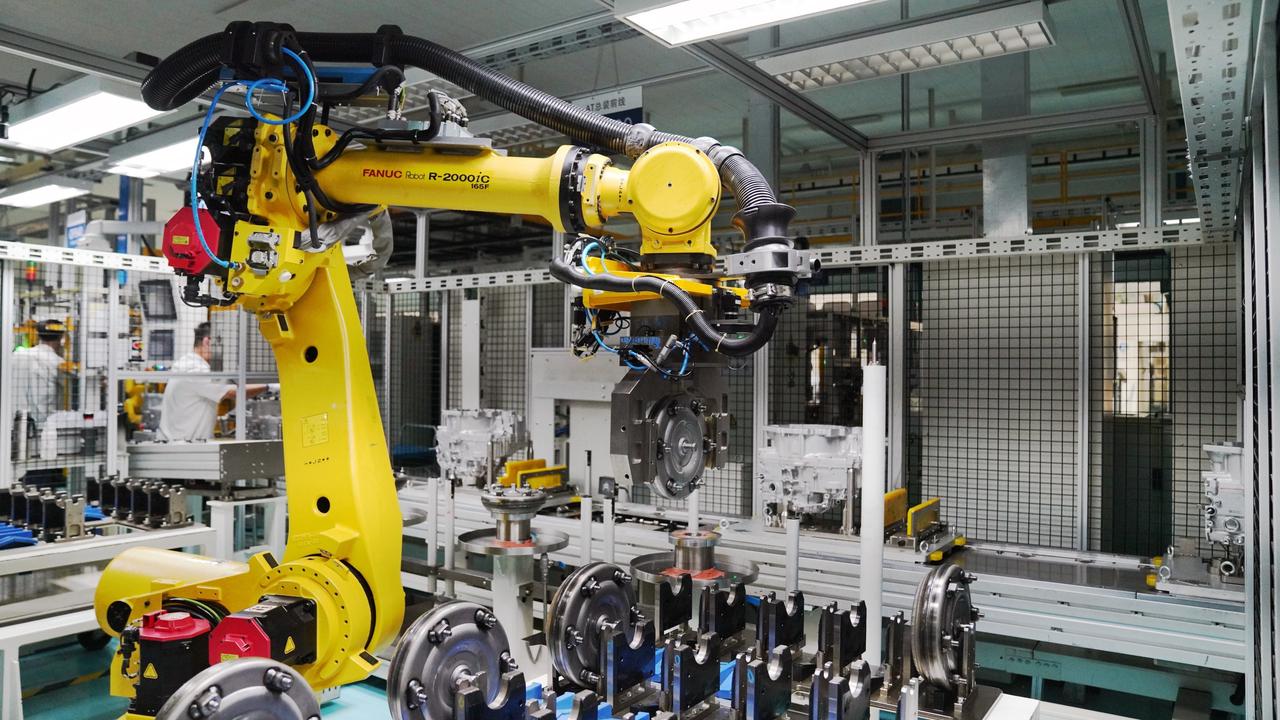 Yellow FANUC robot arm handling parts in factory.