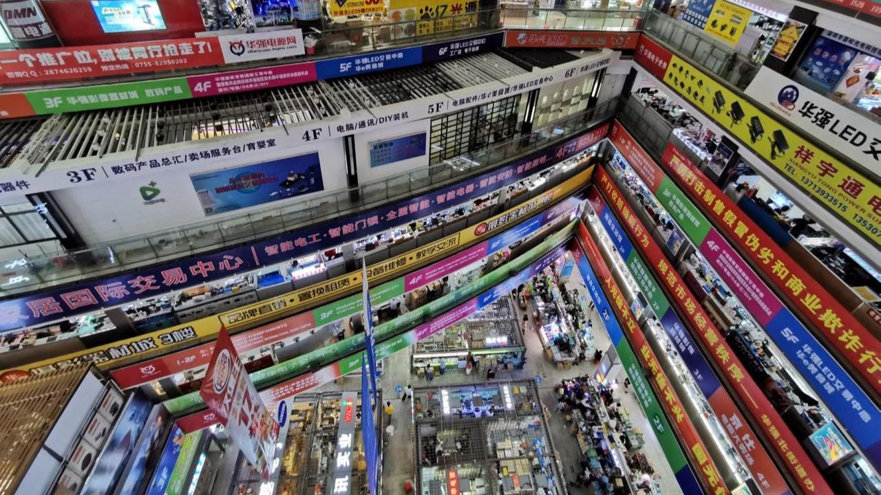 Interior of Huaqiang Electronics Market: multi-floor stalls with colorful signs, busy shoppers.