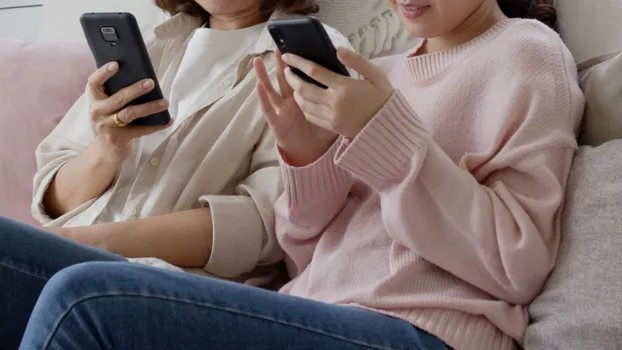Two women on a couch, each using a black smartphone.
