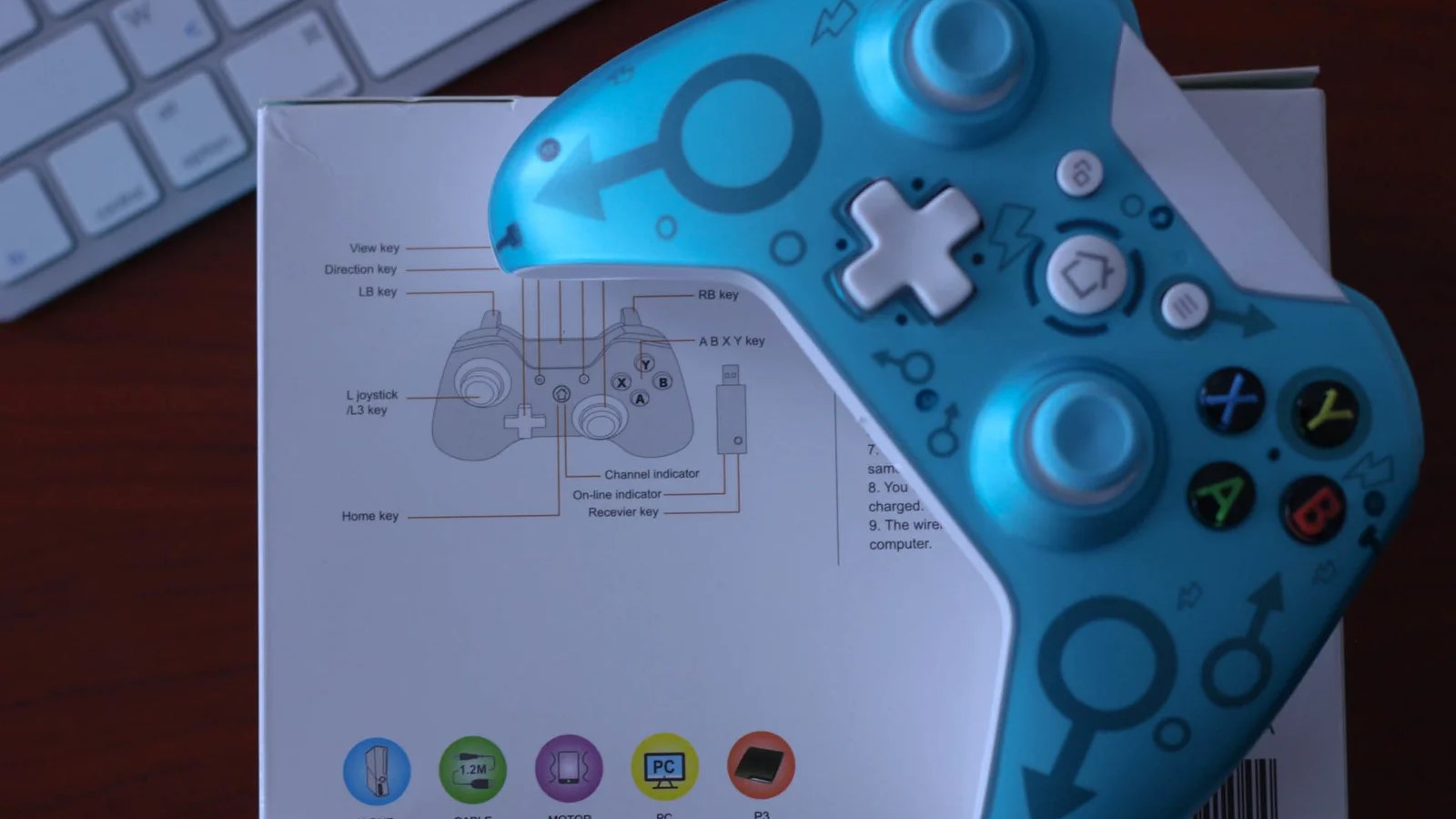 Turquoise game controller resting on its labeled packaging box, with a keyboard in the background.