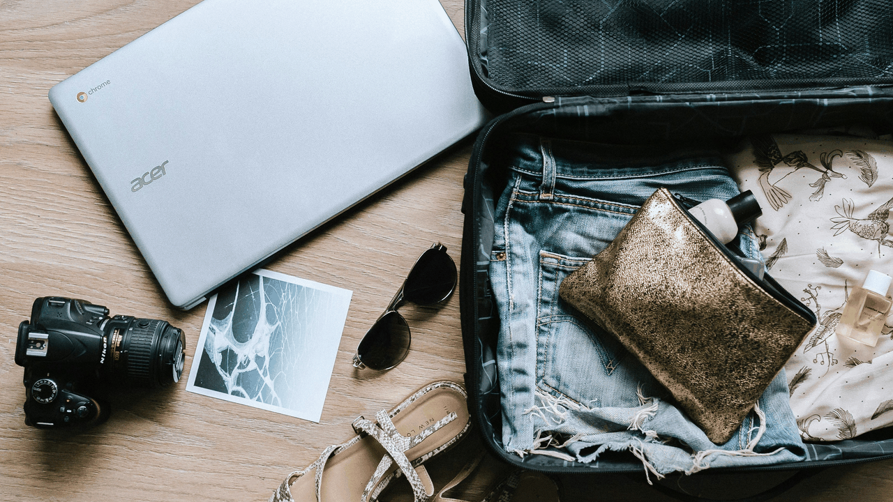 Packing for travel: Laptop, camera, clothes, and accessories by open suitcase.