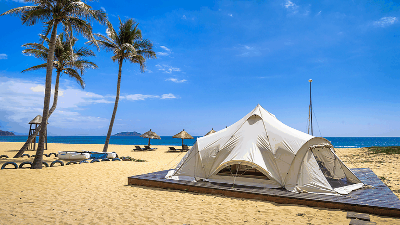 A stunning view of Yalong Bay beach in Sanya, featuring soft white sand, clear turquoise waters, and lush green palm trees lining the shore under a bright blue sky